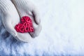 Female hands in white knitted mittens with entwined vintage romantic red heart on snow background. Love and St. Valentine concept