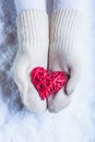 Female hands in white knitted mittens with entwined vintage romantic red heart on snow background. Love and St. Valentine concept