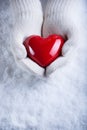 Female hands in white knitted mittens with a glossy red heart on a snow winter background. Love and St. Valentine cozy concept Royalty Free Stock Photo