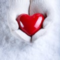 Female hands in white knitted mittens with a glossy red heart on a snow winter background. Love and St. Valentine cozy concept