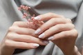 Female hands with white nail design. Female hands holding pink autumn flower. Woman hands on grey fabrick background