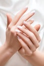 Female hands with white nail design. White nail polish manicured hands. Woman hands on white fabric background