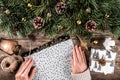 Female hands wrapping a Christmas gift on holiday wrapping on wooden background with fir branches, gold decorations. Royalty Free Stock Photo