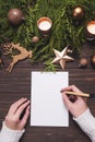 Female hands write Christmas postcard or wishlist on wooden background.