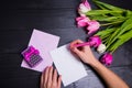 Female hands writing on clear paper with gift box and bouquet of