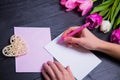 Female hands writing on clear paper with wicker heart and bouquet of tulips Royalty Free Stock Photo