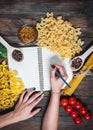 Female hands writing notepad. spices, pasta and vegetables around notebook on wooden table. Mockup