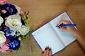 Bouquet of roses on wooden background, notebook and pencil in woman hand. Female hands writing in open notebook and bouquet of Royalty Free Stock Photo