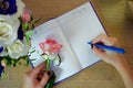 Female hands writing in open notebook and bouquet of roses on old wooden table. Top view. Planning notebook with pen, woman makes Royalty Free Stock Photo