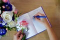 Female hands writing in open notebook and bouquet of roses on old wooden table. Top view. Planning notebook with pen, woman makes Royalty Free Stock Photo