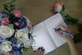 Female hands writing in open notebook and bouquet of roses on old wooden table. Top view. Planning notebook with pen, woman makes Royalty Free Stock Photo