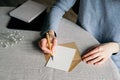 Female hands writing wedding invitation card. Blank paper card, envelope, notebook, gypsophila on table with linen tablecloth.