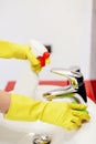 Female hands with yellow rubber gloves cleaning tap with sponge. Royalty Free Stock Photo