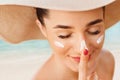 Female in hat applying moisturizing lotion on skin. Beautiful Young woman with sun cream on face.Skin care. Sun protection.