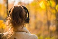 Female in headphones standing near big maple tree in park and listen sounds or music in the autumn forest. Concept.