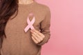 Female health check awareness. Closeup of young woman in pullover holding pink ribbon, symbol of breast cancer