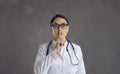 Female healthcare professional or doctor puts her index finger to her lips demanding silence.