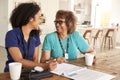 Female healthcare worker sitting at table smiling with a senior woman during a home health visit Royalty Free Stock Photo