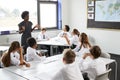 Female High School Tutor Standing By Tables With Students Wearing Uniform Teaching Lesson Royalty Free Stock Photo