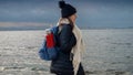 Female hiker, equipped with a backpack and thermos, exploring a rocky sea beach on a cold, cloudy day. Addition to any travel,