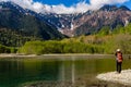 Female hiker next to a pond in front of towering, snowcapped mountains (Kamikochi, Japan