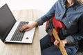 Casually dressed young woman with guitar playing songs in the room at home. Laptop on table. Online guitar lessons concept. Male g Royalty Free Stock Photo