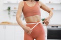 Female holding measuring tape along waistline in kitchen