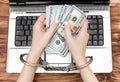 Female holding money in hands which are locked up by handcuffs over laptop. Top view Royalty Free Stock Photo