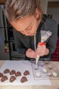 A female home baker pours melted chocolate using a piping bag into a candy mold to make homemade chocolate candies