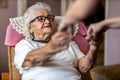 Female home carer supporting old woman to stand up from the armchair Royalty Free Stock Photo