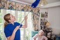 Female Home Help Cleaning House As She Dusts And Talks To Senior Woman