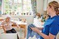 Female Home Help Cleaning House Doing Washing Up In Kitchen Whilst Chatting With Senior Woman