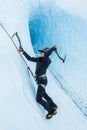 Female ice climber swinging an ice tool behind her head. Behind her is a massive ice cave on the Matanuska Glacier in Alaska