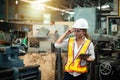 Female industrial engineer wearing a white helmet while standing in a heavy industrial factory behind she looking of working at