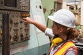 Female industrial worker working and checking machine in a large industrial factory with many equipment