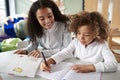 Female infant school teacher working one on one with a young schoolgirl sitting at a table writing in a classroom, front view, clo Royalty Free Stock Photo