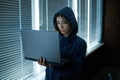 Female internet hacker in hood works on laptop