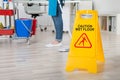Female Janitor Mopping Wooden Floor With Caution Sign