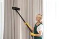 Female janitor removing dust from curtain