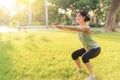 Female jogger. Fit young Asian woman with green sportswear squatting in park before running and enjoying a healthy outdoor. Royalty Free Stock Photo