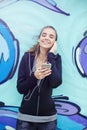 Female jogger listening music on mobile phone in front of graffiti wall