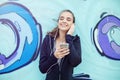 Female jogger listening music on mobile phone in front of graffiti wall