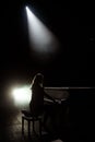 Female keyboards player on stage during concert, backlight