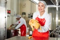 Female kitchen worker with raw chicken carcass in her hands and meat prepared for sale