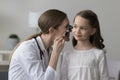 Female laryngologist in white examining little girl ear