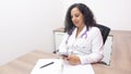 Female latin female doctor sitting looking at her phone in her office with stethoscope on her neck typing on her smartphone
