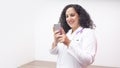 Female latin female doctor smiling standing looking at her phone in her office with stethoscope on her neck typing on her phone Royalty Free Stock Photo