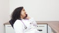 Female latin female doctor sitting relax in her consulting room with stethoscope on her neck talking to her smart phone