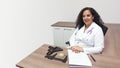 Female latin female doctor sitting smiling in her office with stethoscope on her neck seen from above