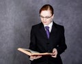 Female lawyer reads a big book with serious expression, woman in a man`s suit, tie and glasses